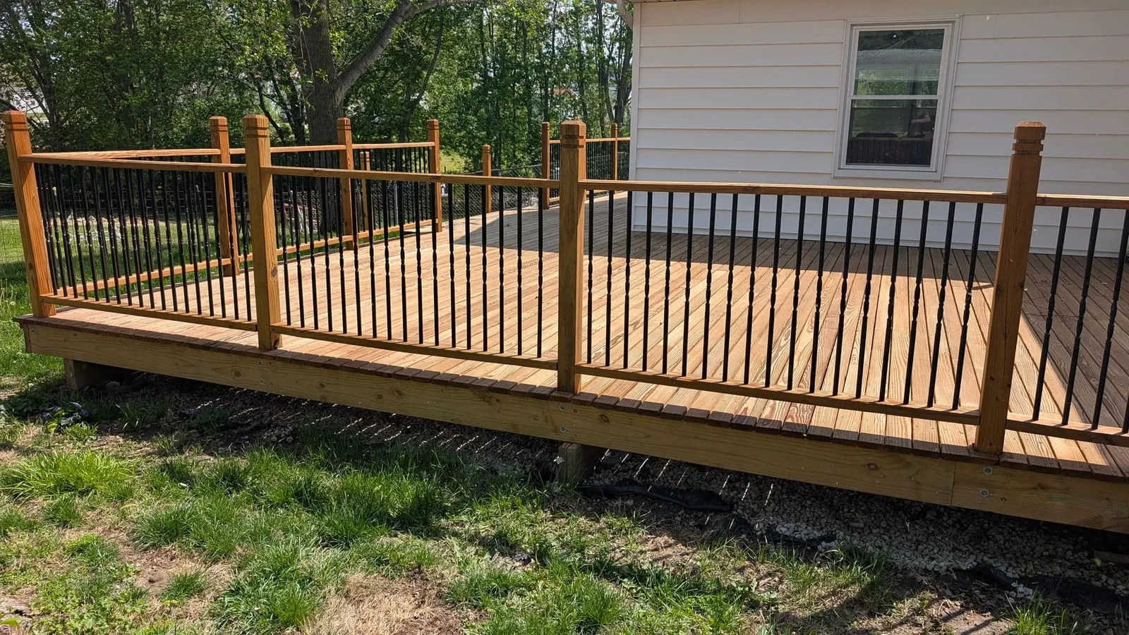 New wood deck with wooden posts and black metal balusters beside a white house