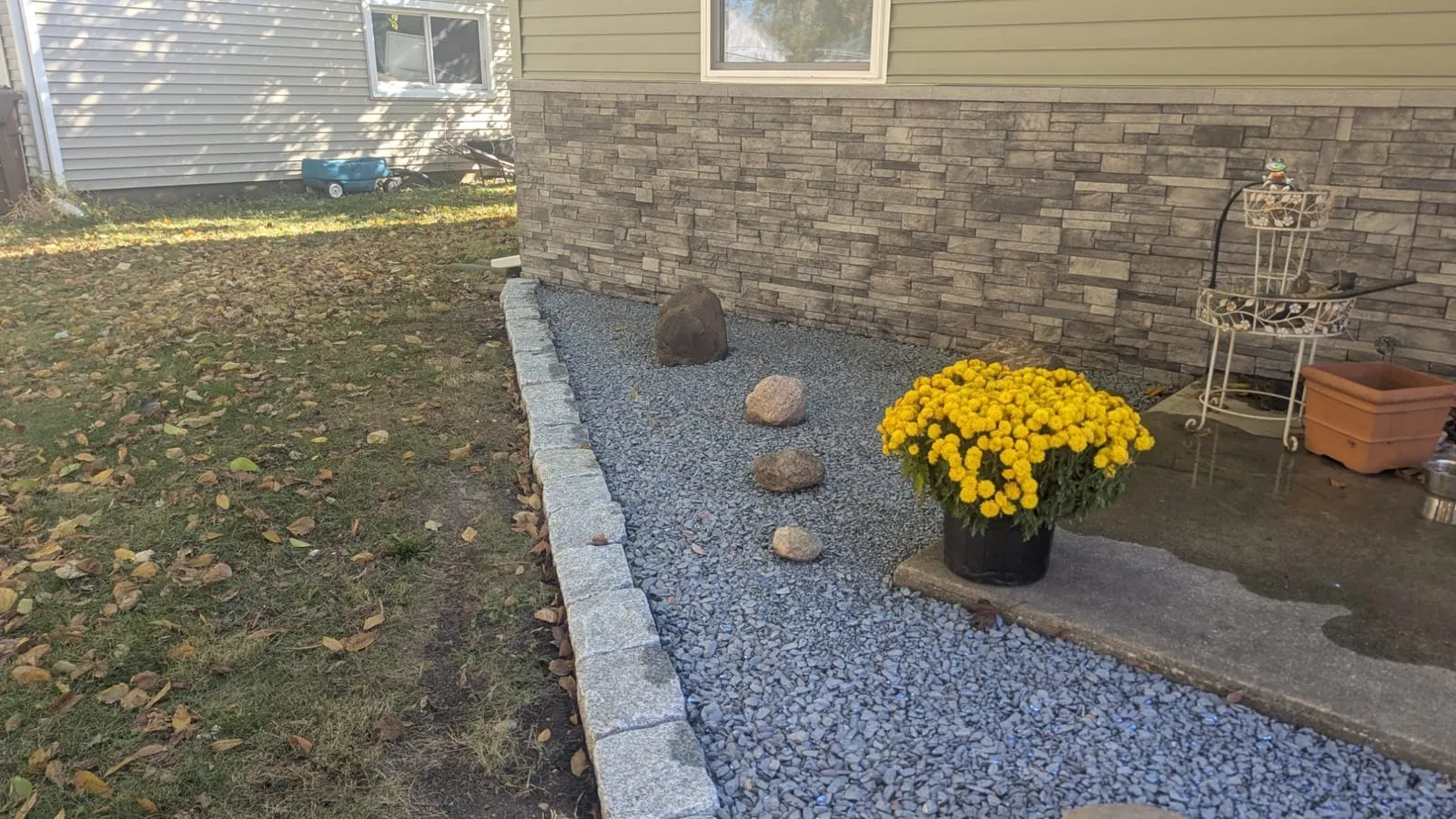 Gravel bed with boulders and potted mums beside a front step, edged in stone