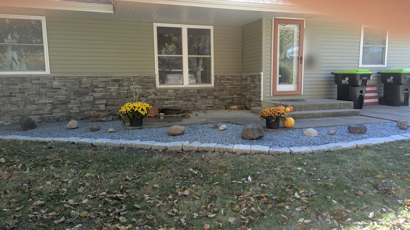 Finished gray gravel bed across the front of a house, with boulders and a curved stone edging border