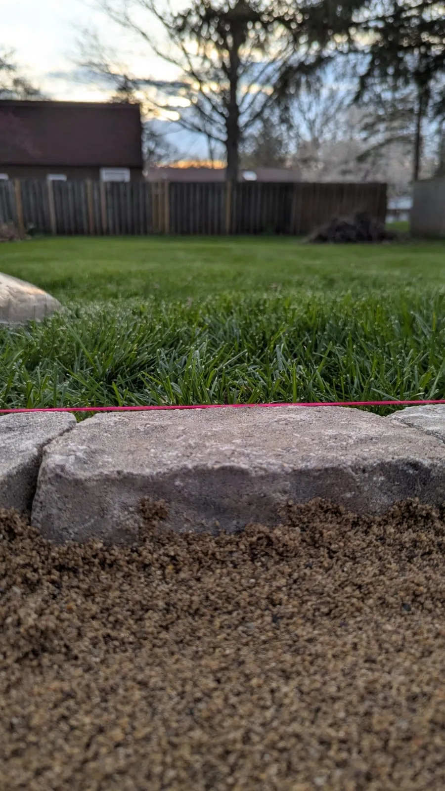 Close-up of a stone edging block set on a sand base, lined up to a pink string line along the lawn